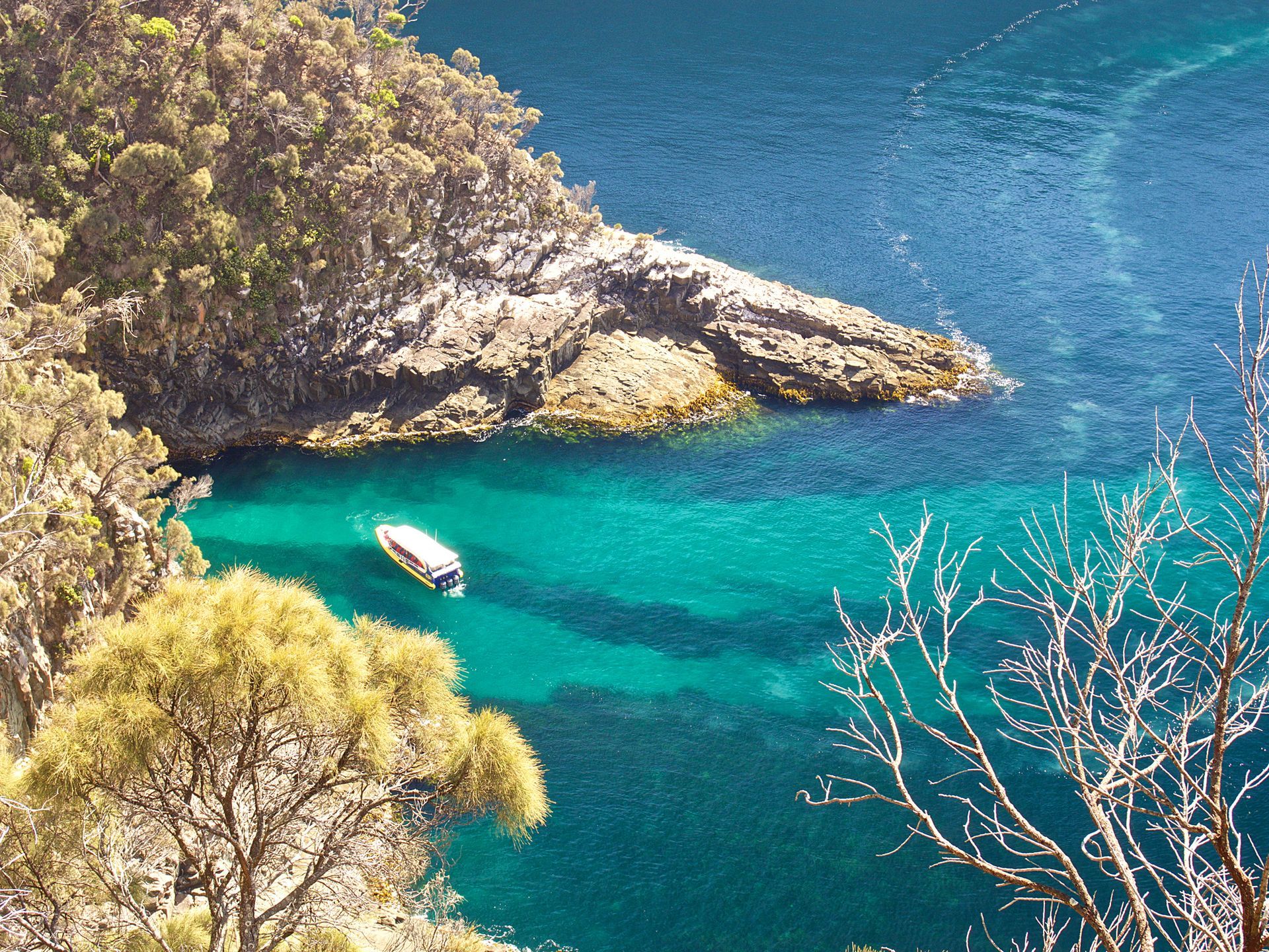 A small boat floating in clear turquoise water near a rocky shoreline.