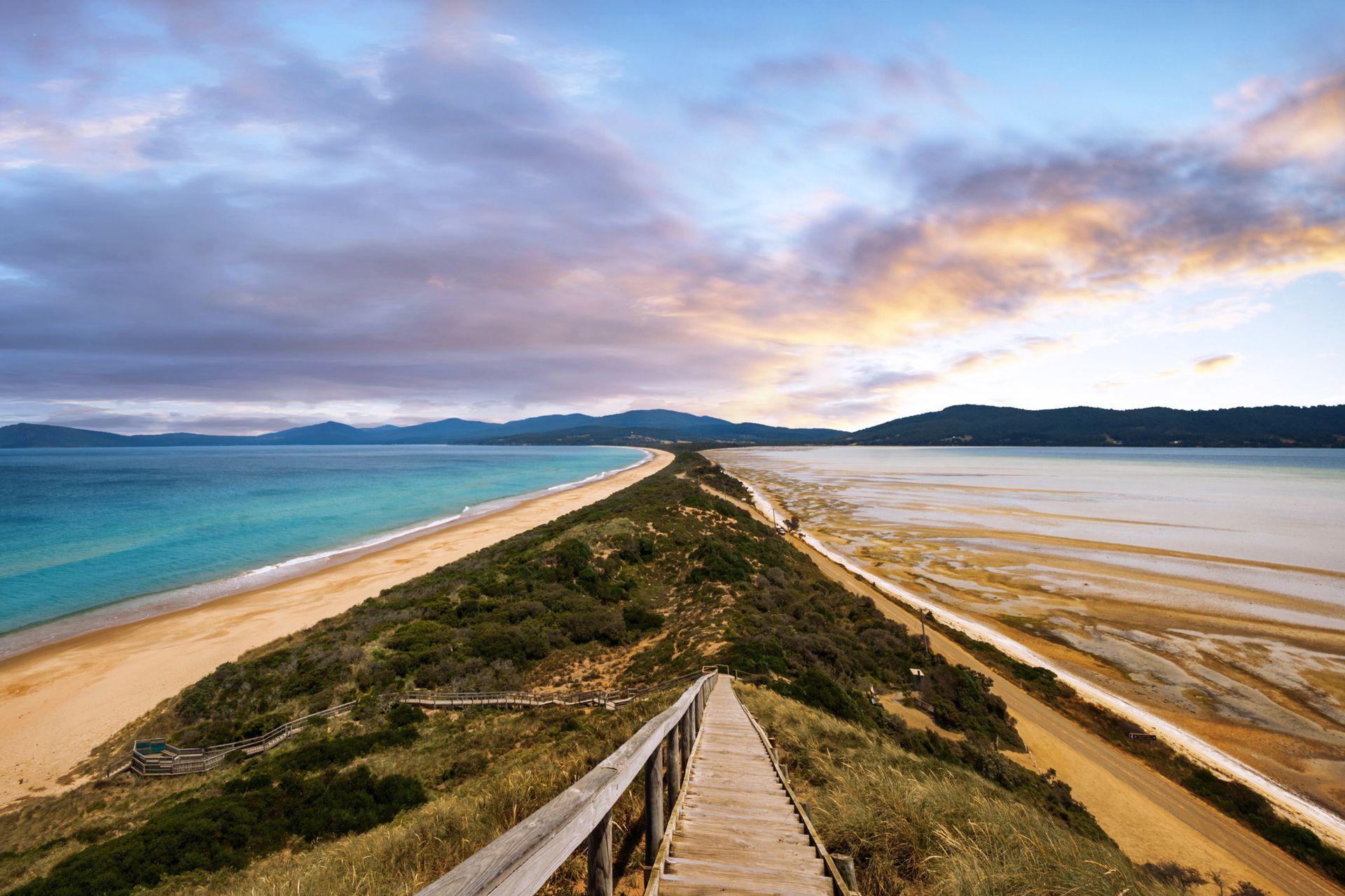 A wooden walkway leading to a beach and a body of water.