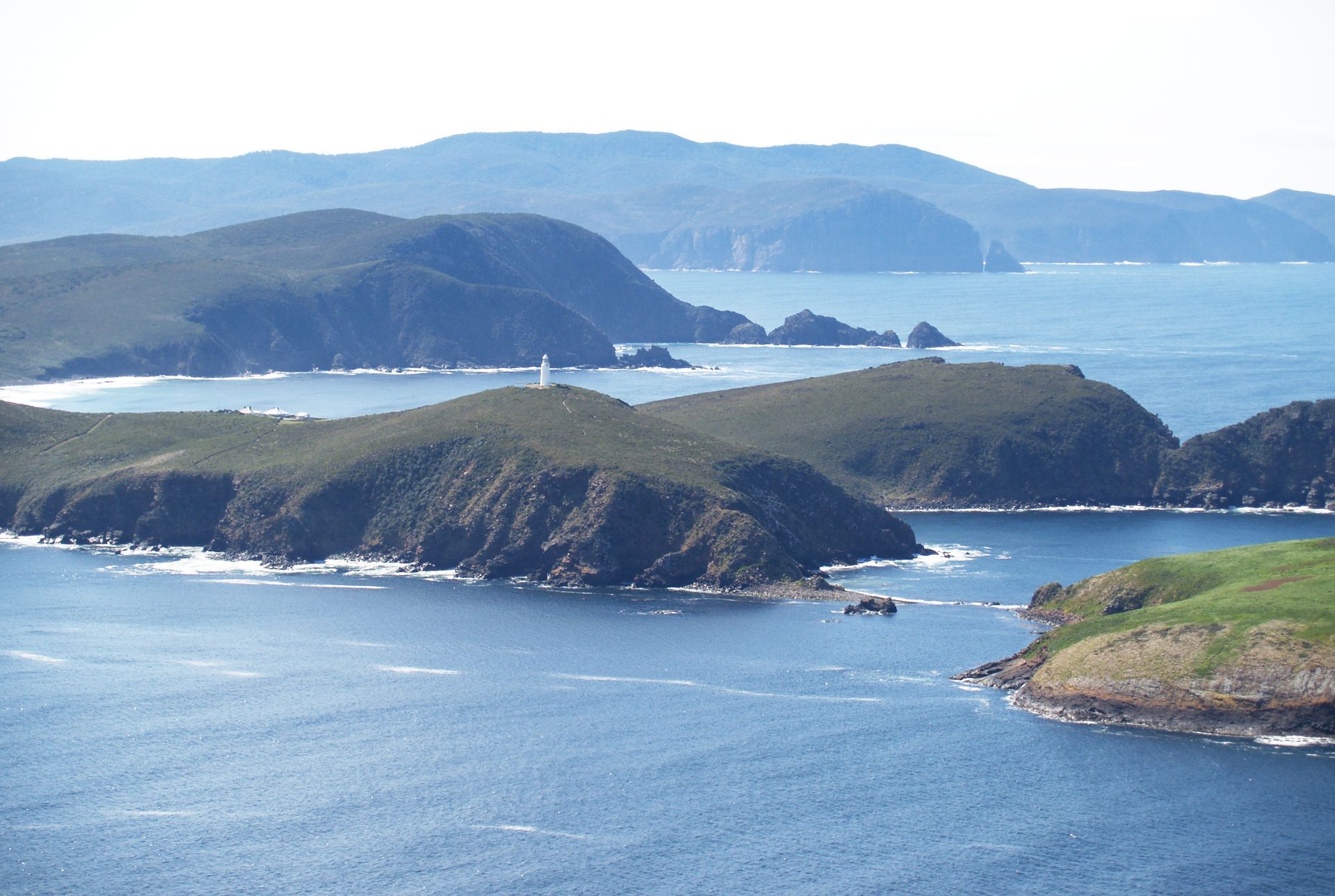 Island landscape with dark green hills, blue water, and distant mountains.