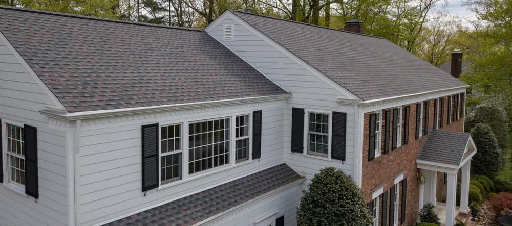 An aerial view of a large white house with a gray roof and black shutters.