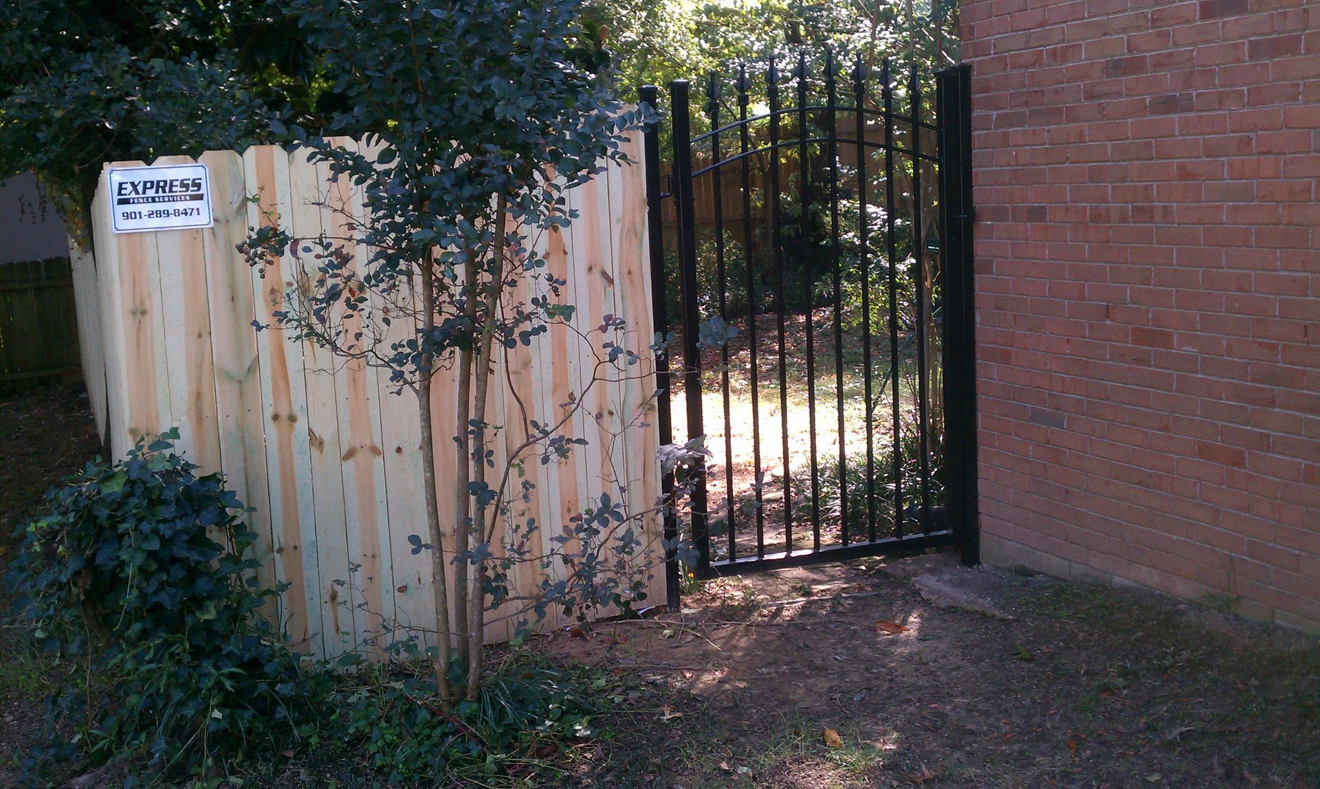 A wooden fence with a metal gate in front of a brick building