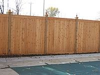 A wooden fence surrounds a swimming pool with a green cover.