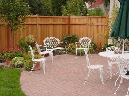A wooden fence surrounds a patio with tables and chairs