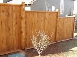 A wooden fence with a bush in the middle of it in front of a house.