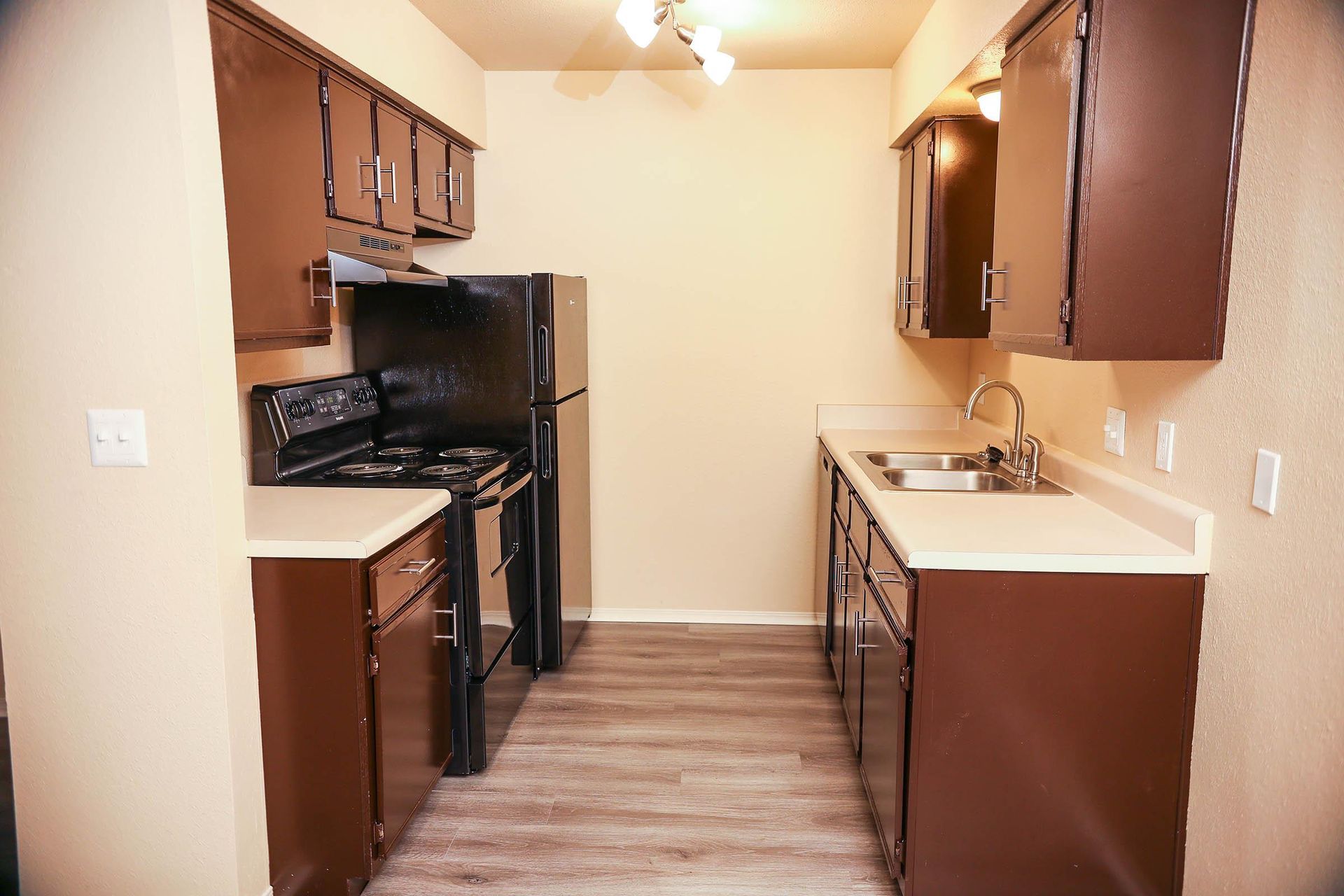 A narrow kitchen with brown cabinets, beige countertops, and black appliances.