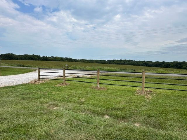 Grassy field with a wooden fence, gravel path, and cloudy sky