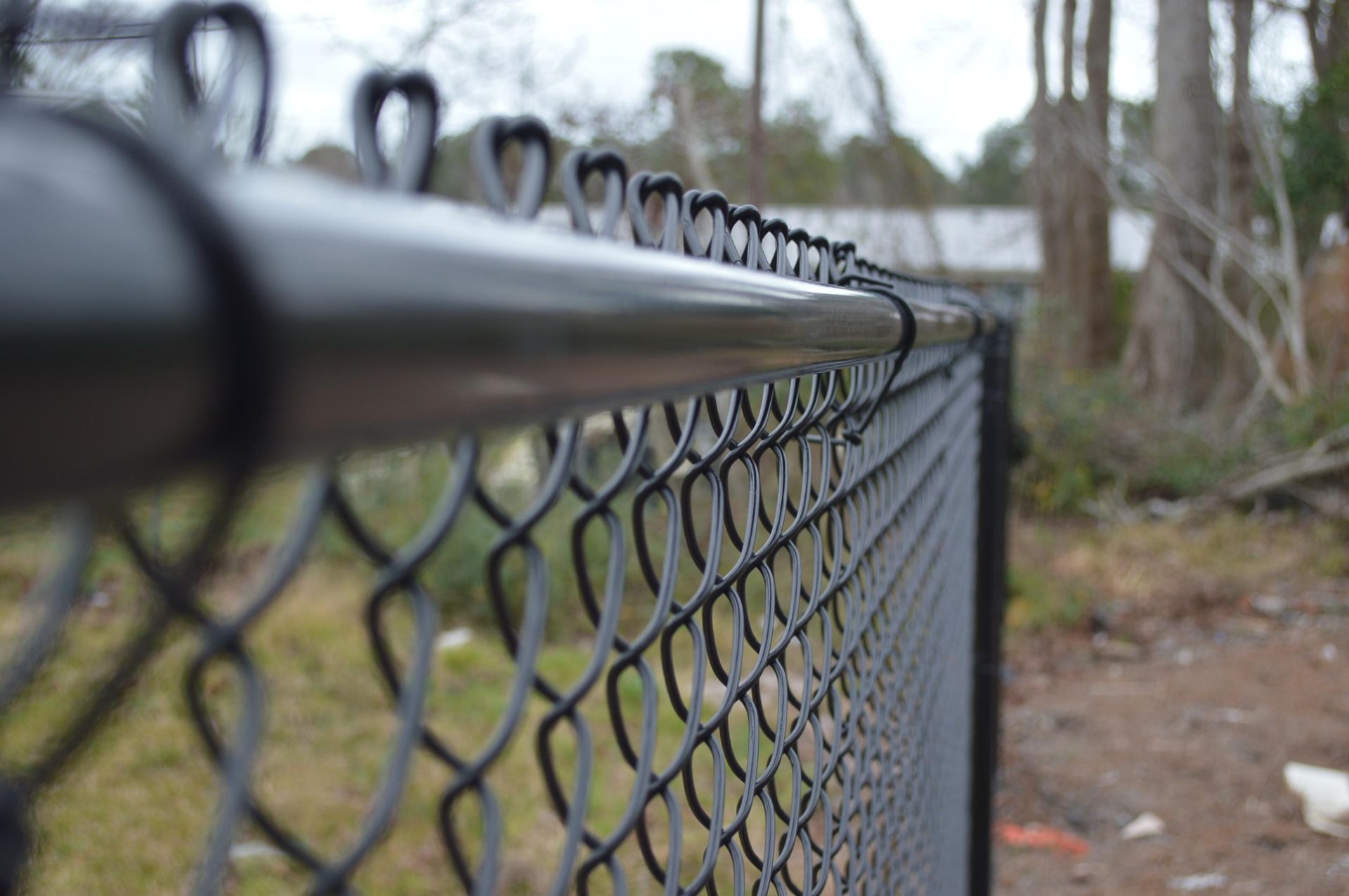 Close-up of a black chain-link fence with a blurred outdoor background and bare trees