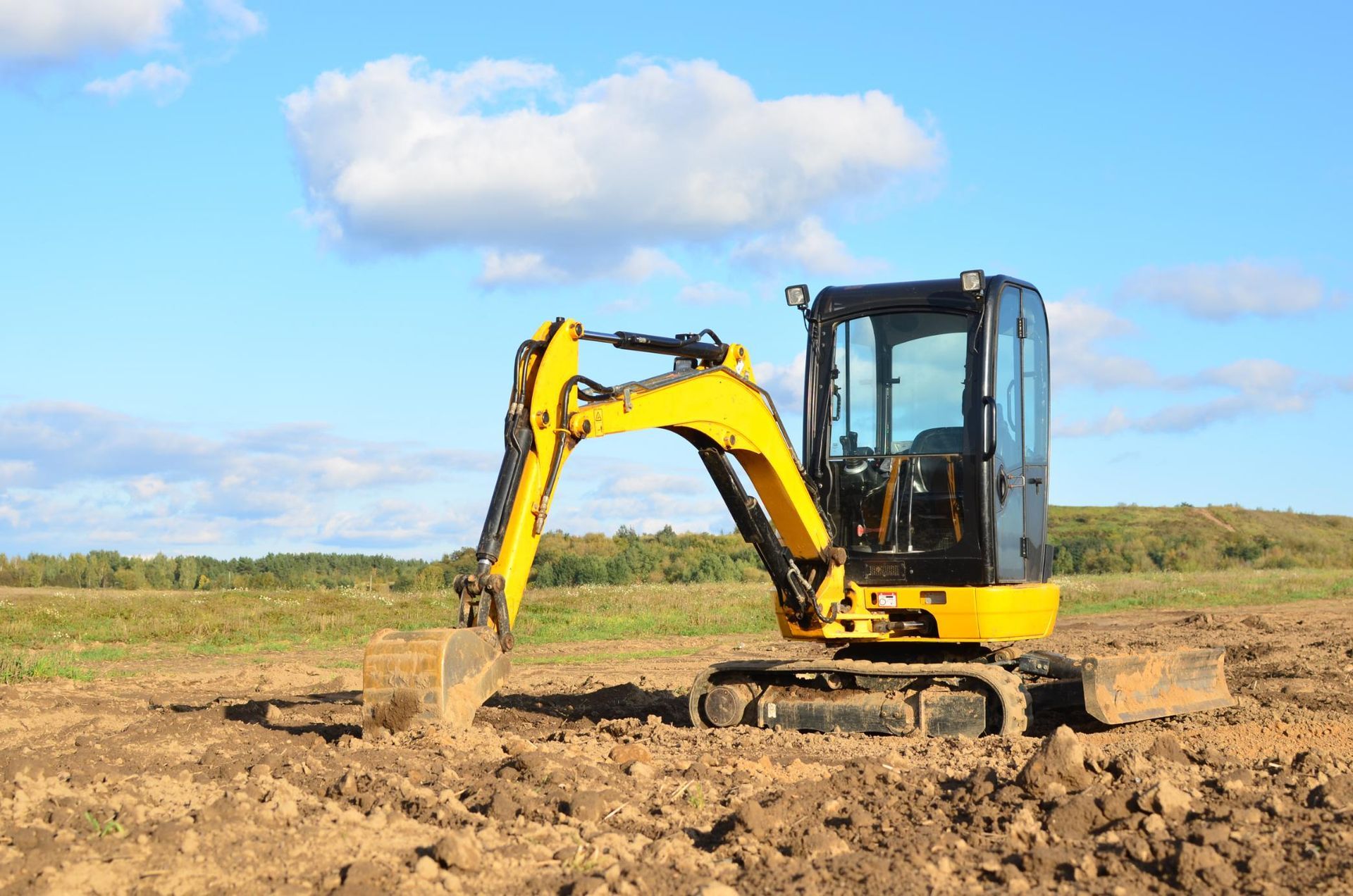 Yellow excavator working on a dirt site under a blue sky