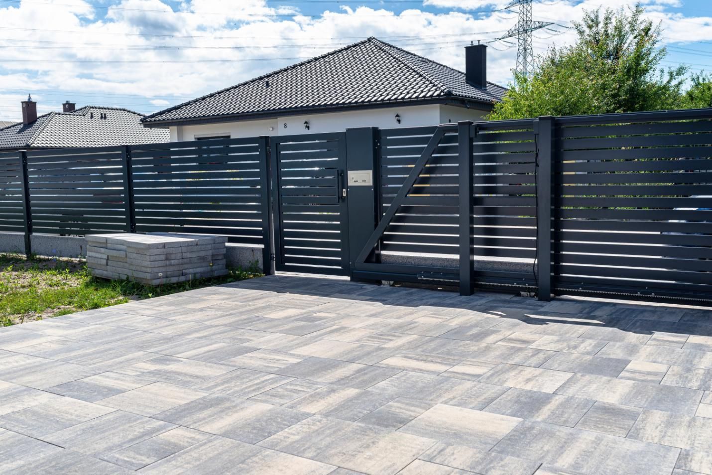Black slatted fence and gate in front of a gray house with a paved driveway