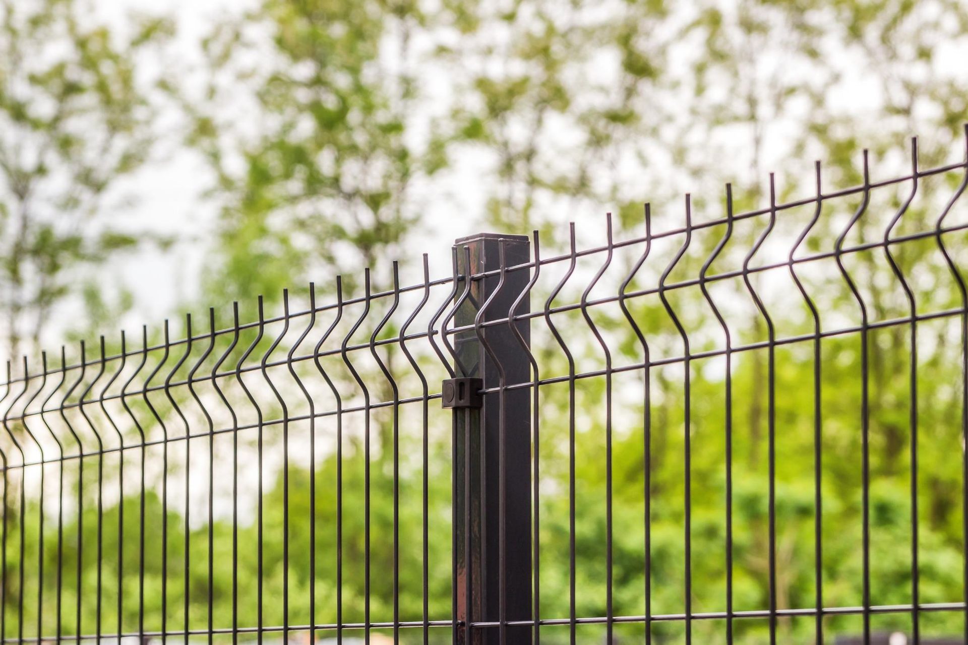 Black metal fence with barbed top against a green outdoor background