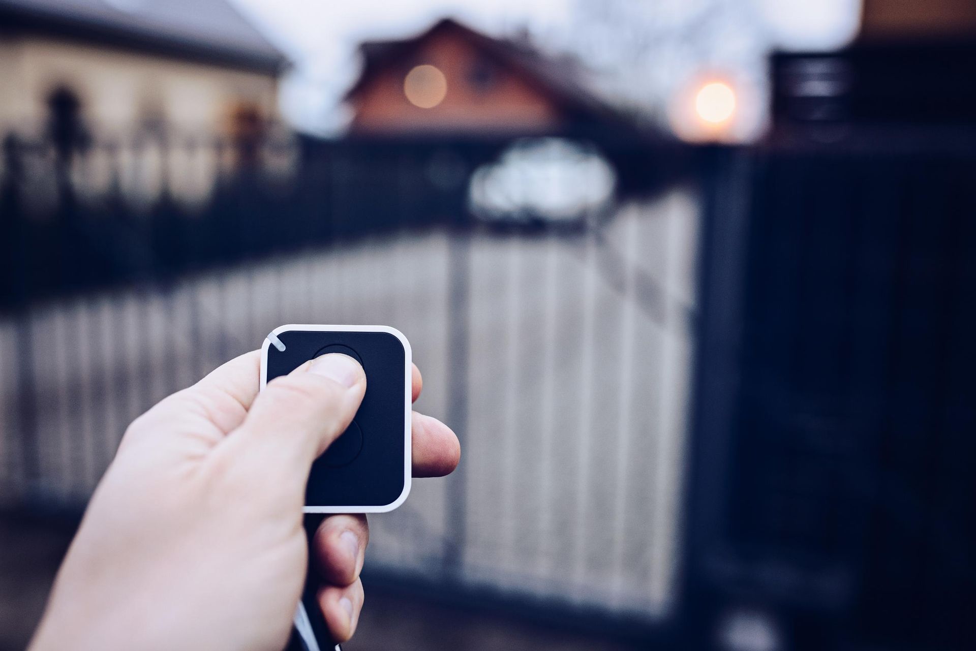 Hand holding a key fob toward a blurred driveway gate at dusk
