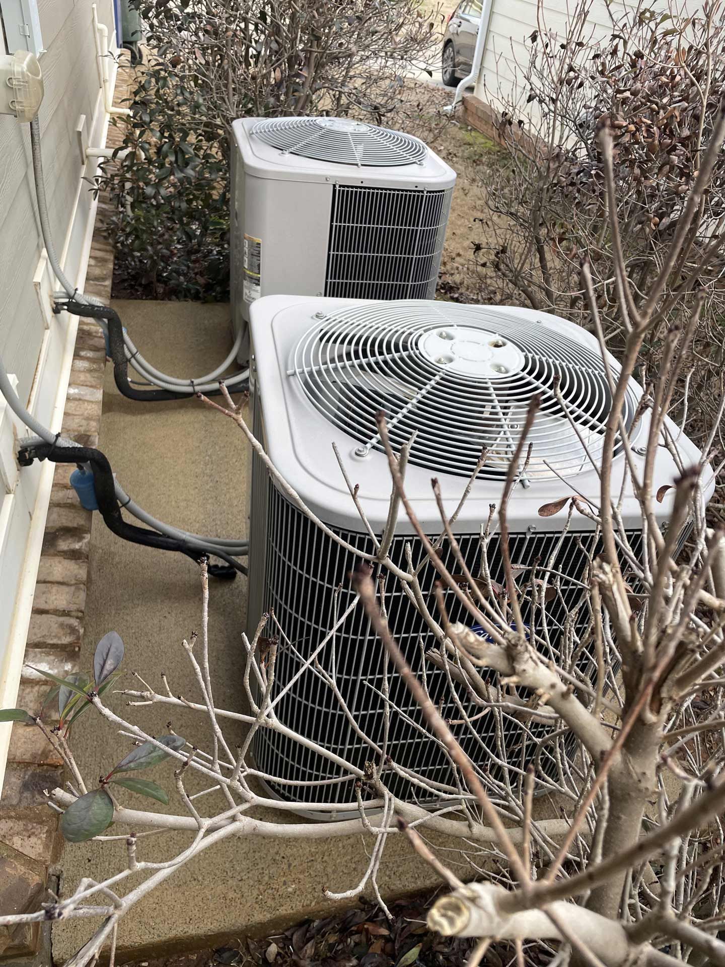 Two air conditioners are sitting next to each other on the side of a house
