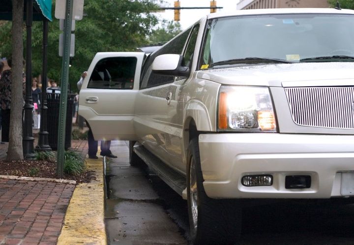 White limousine parked on a city street, door open, person exiting the vehicle.