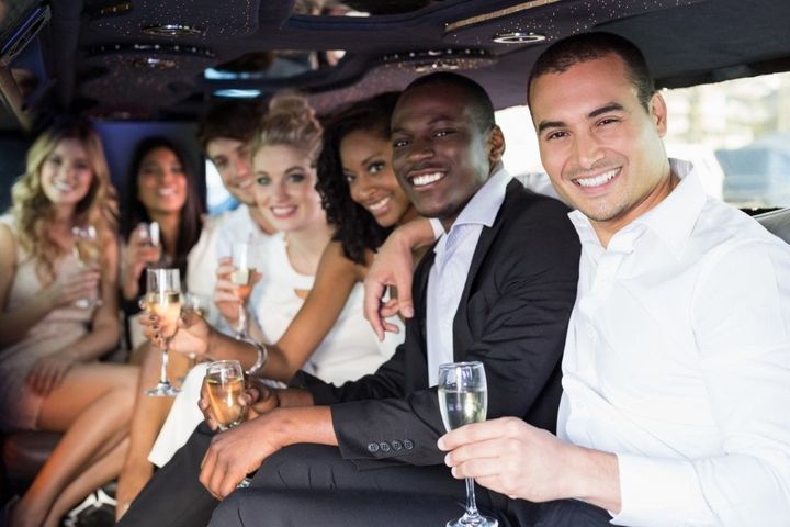 Group of diverse people smiling and holding champagne flutes inside a limousine. They are celebrating, wearing formal attire.
