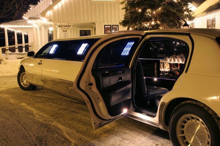 A white limousine with an open door parked outside a house decorated for a winter holiday.
