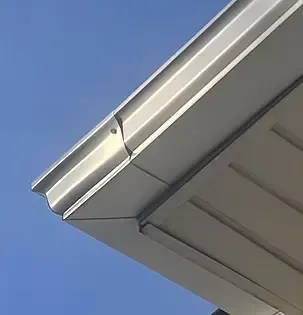 Close-up of a silver metal roof edge with a gutter, against a blue sky.
