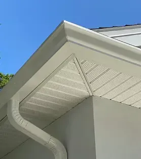 White house corner with gutter, soffit, and siding against a blue sky.