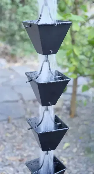 Black metal rain chain with water flowing through square cups.