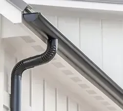 Black rain gutter attached to a white building; a downspout is curved downward.