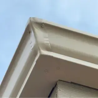 Beige roof corner with visible fasteners against a light blue sky.