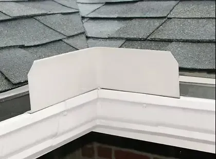 White metal corner flashing installed on a roof with gray shingles and white gutters.