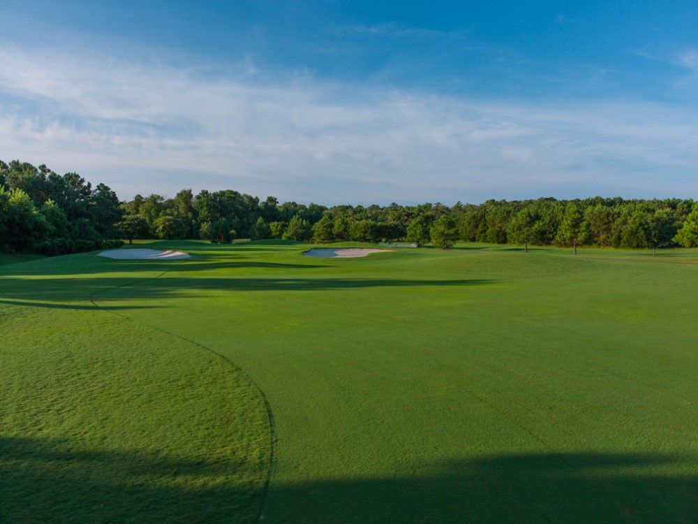 Green golf course with sand traps, trees, and a blue sky.