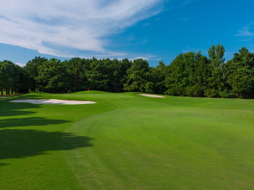 Green golf course with sand traps, lush green grass, and trees under a blue sky.
