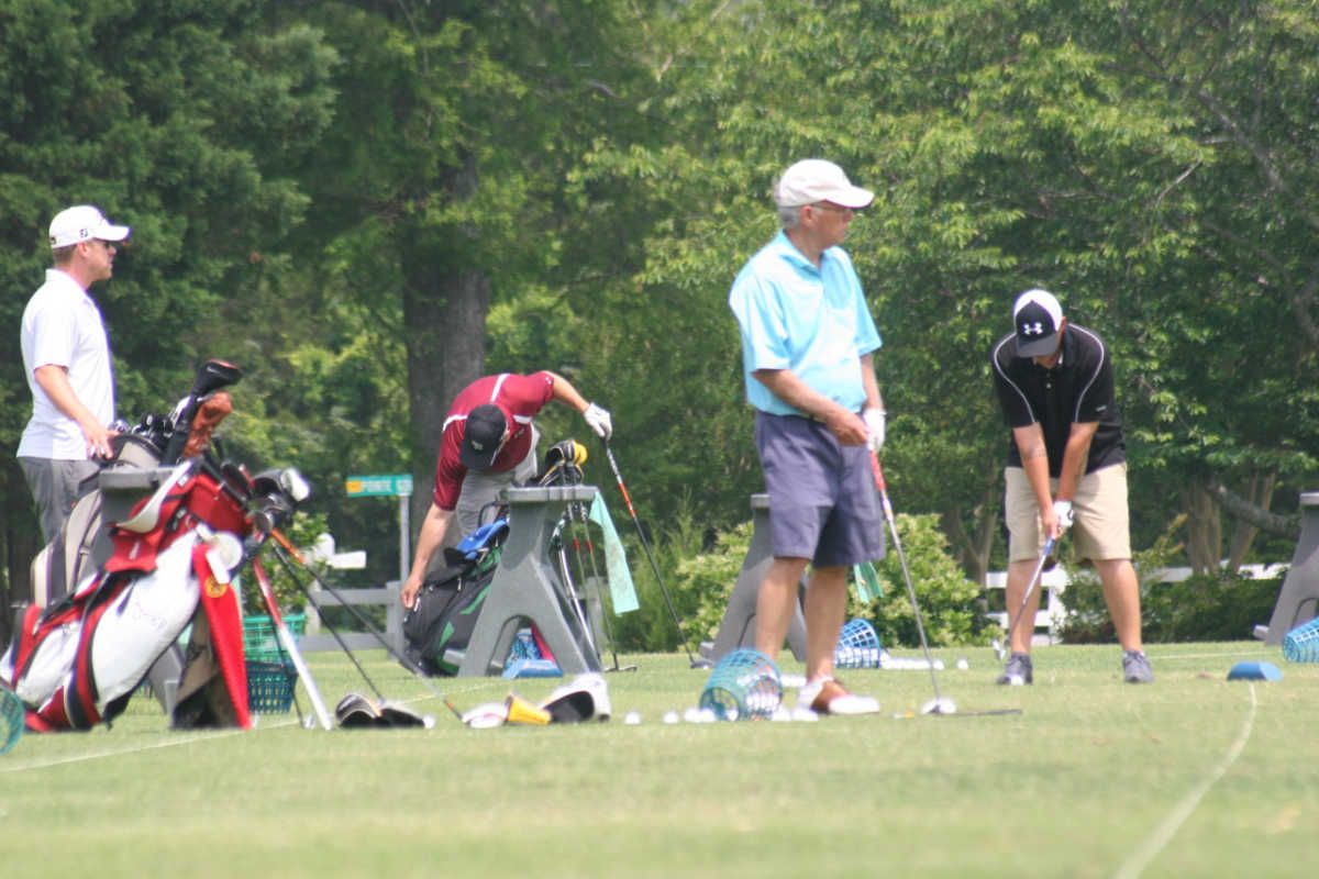 Golfers on a green, preparing to play. One person is teeing off, while others watch or organize their clubs.