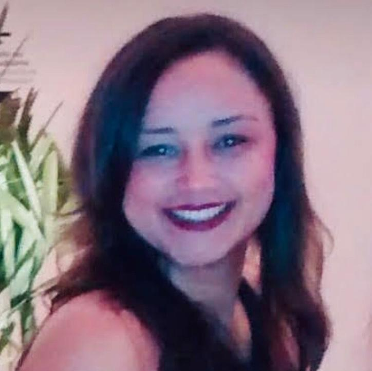 A woman is smiling for the camera in front of a plant.