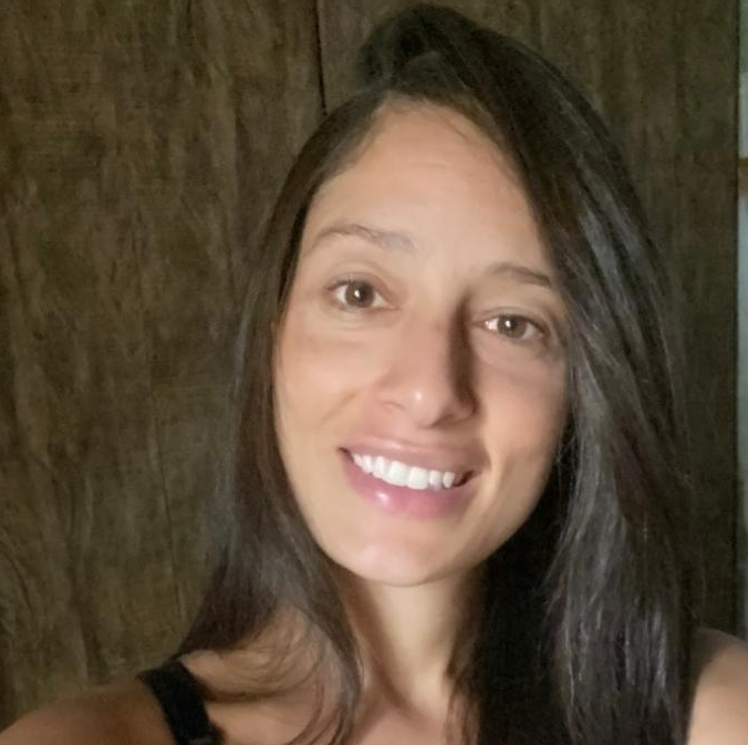 A woman with long dark hair is smiling and wearing a black tank top.