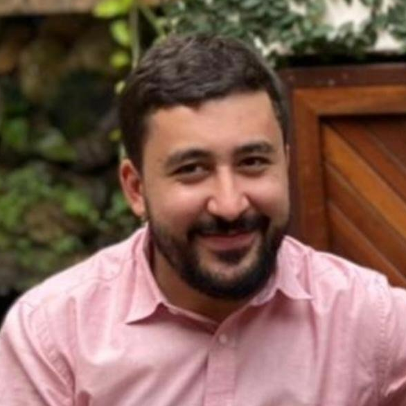 A man with a beard is wearing a pink shirt and smiling