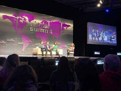 A group of people are sitting in front of a stage at a web summit.