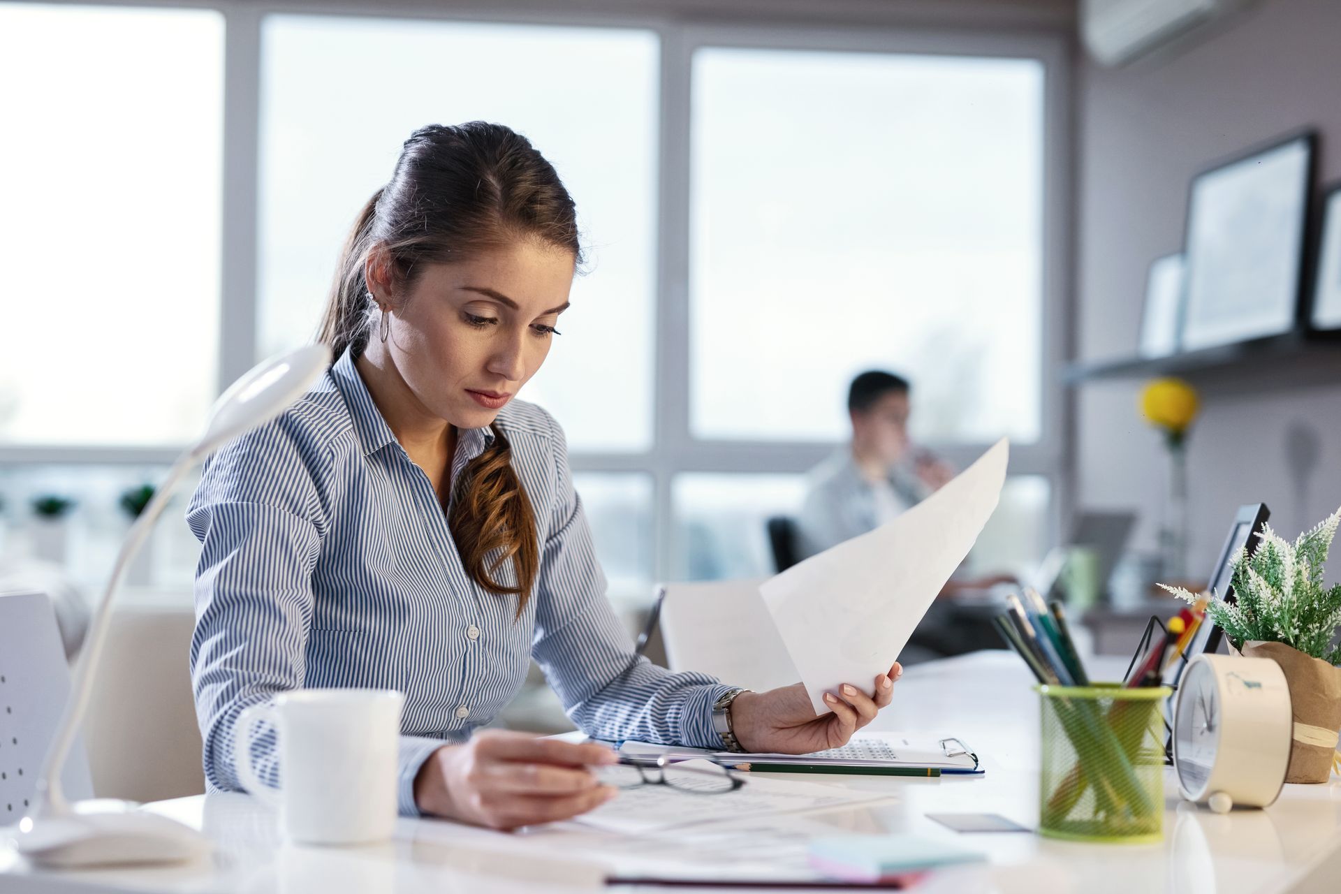 A woman is sitting at a desk reading a piece of paper.