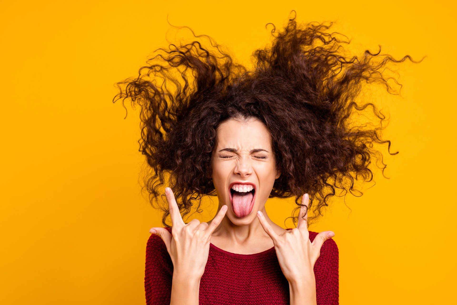 A woman with curly hair is sticking her tongue out and making a rock and roll sign.