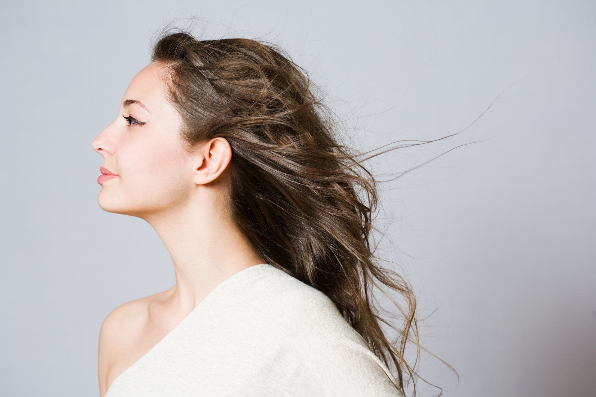 The woman is wearing a white sweater and her hair is blowing in the wind.