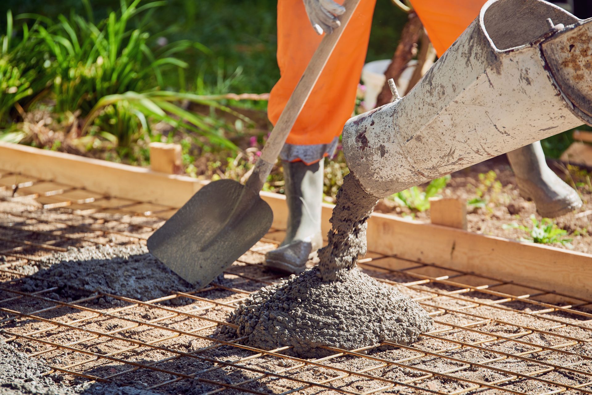 A PARTIAL VIEW OF A CONCRETE POUR WITH A BUILDER HOLDING A SHOVEL.