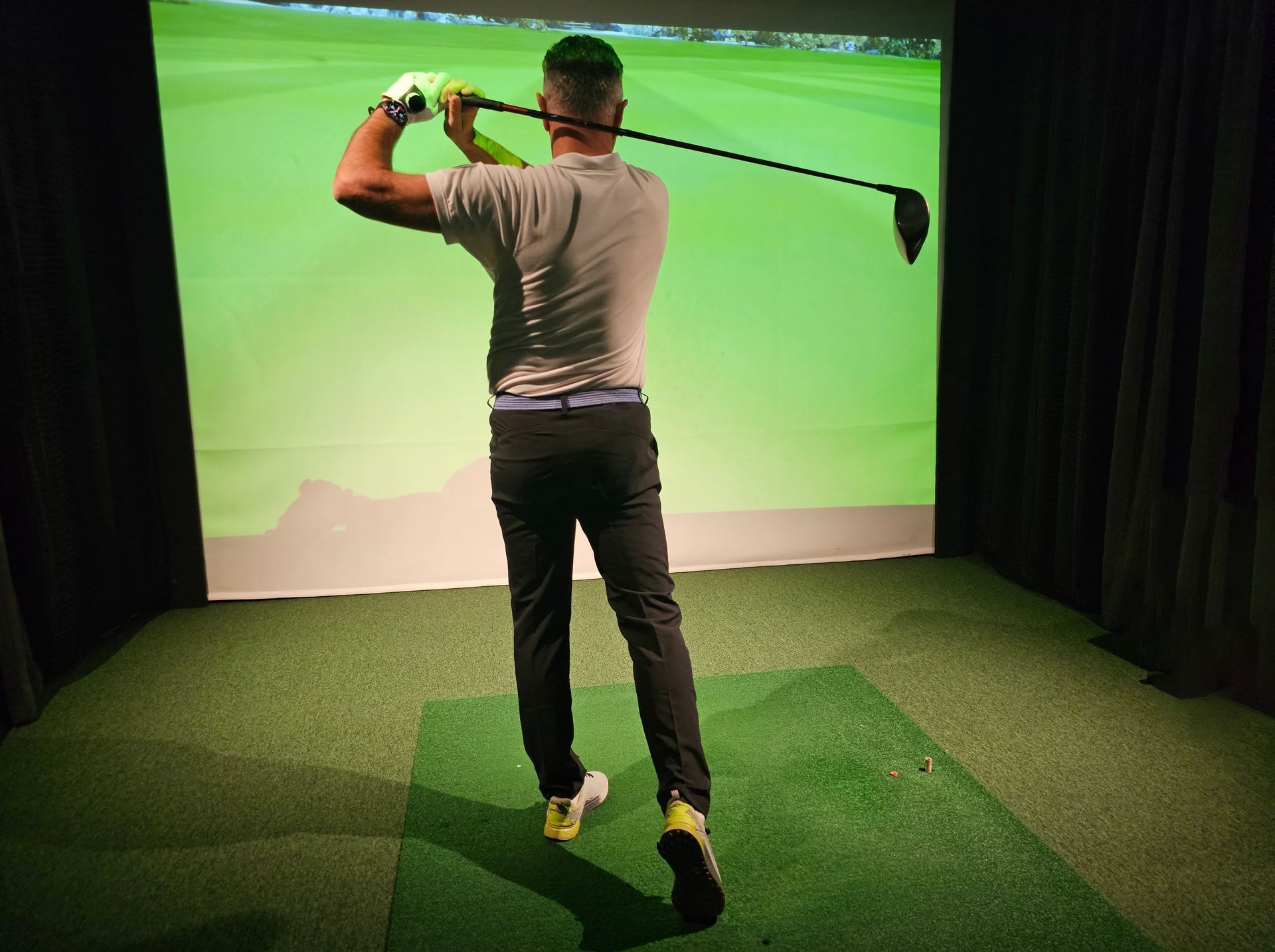 Professional male golfer holding a club playing golf indoors on a golf simulator.