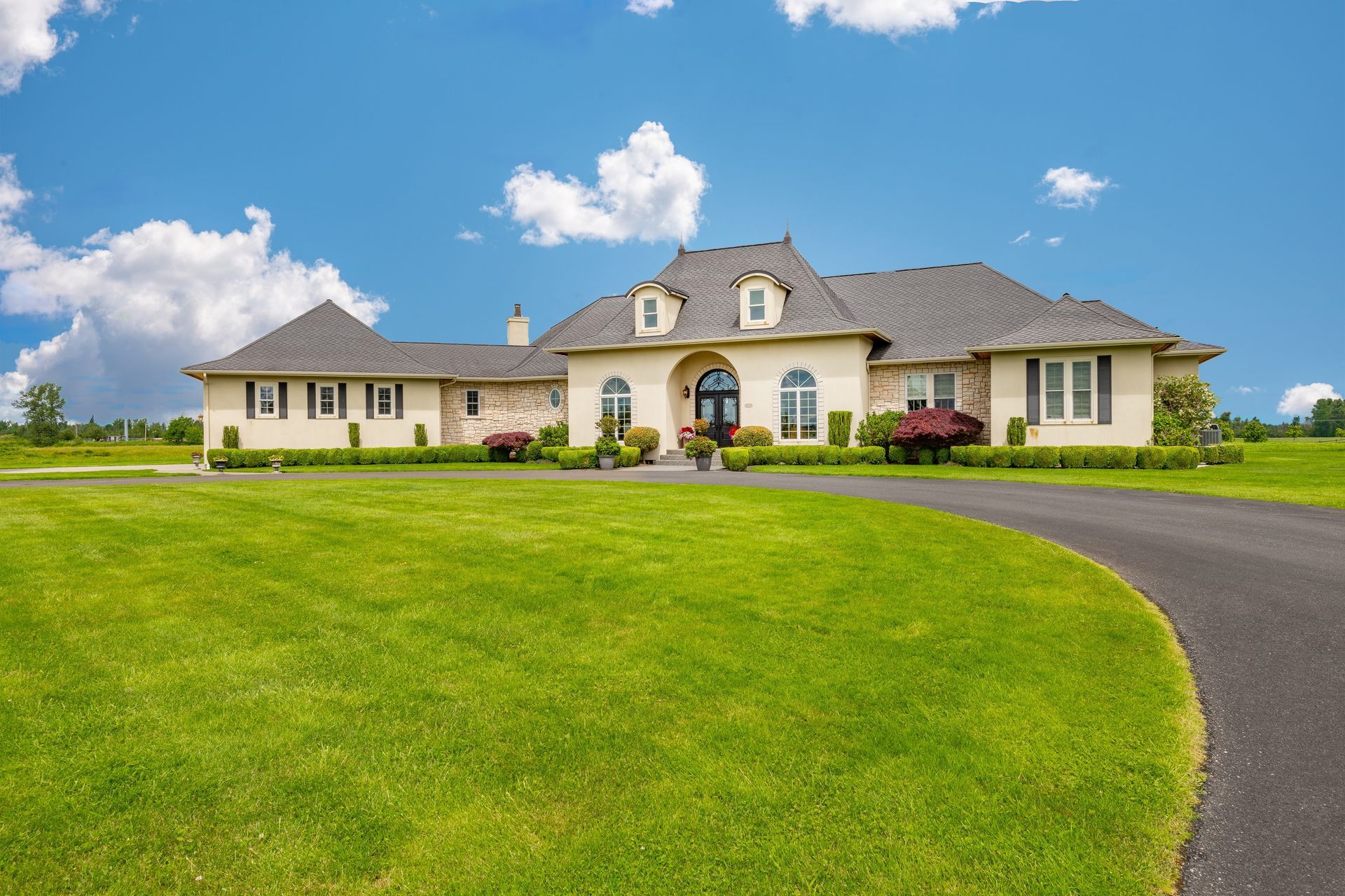 A large white house with a gray roof is sitting on top of a lush green field.