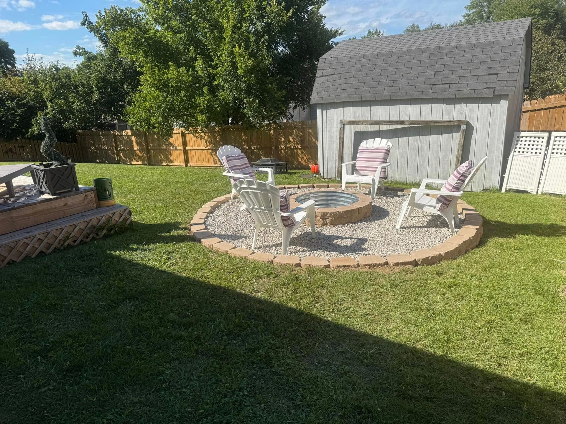 There is a fire pit in the middle of the yard with chairs around it.