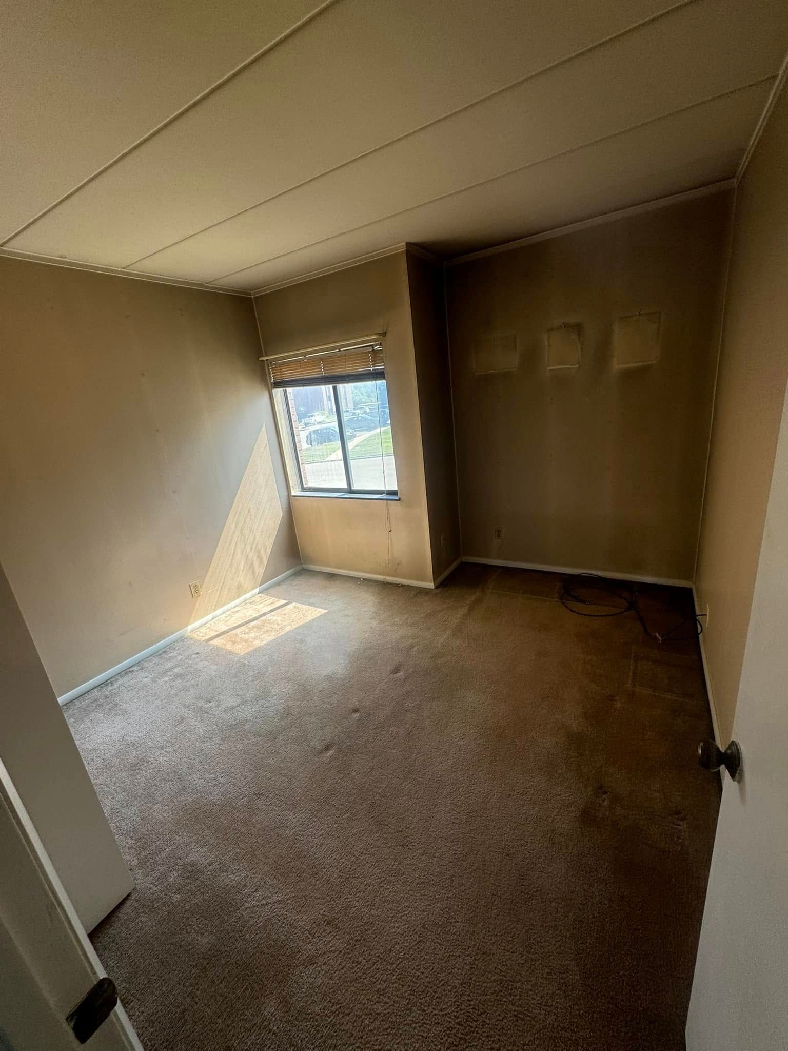 An empty room with a window and a carpeted floor.