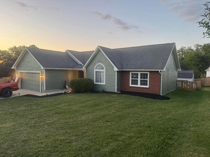 A green house with a gray roof and a red truck parked in front of it.