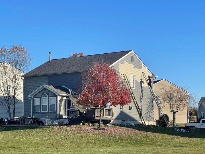 A couple of people are painting a house in a residential area.
