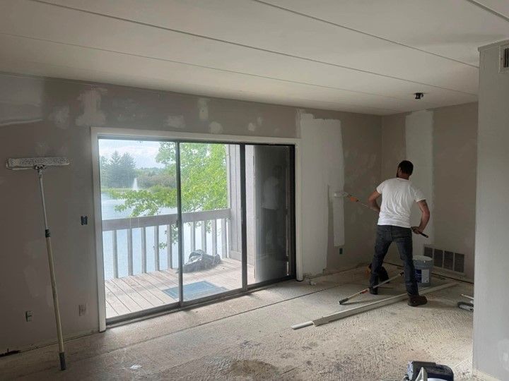 A man is painting a wall in a room with a sliding glass door.
