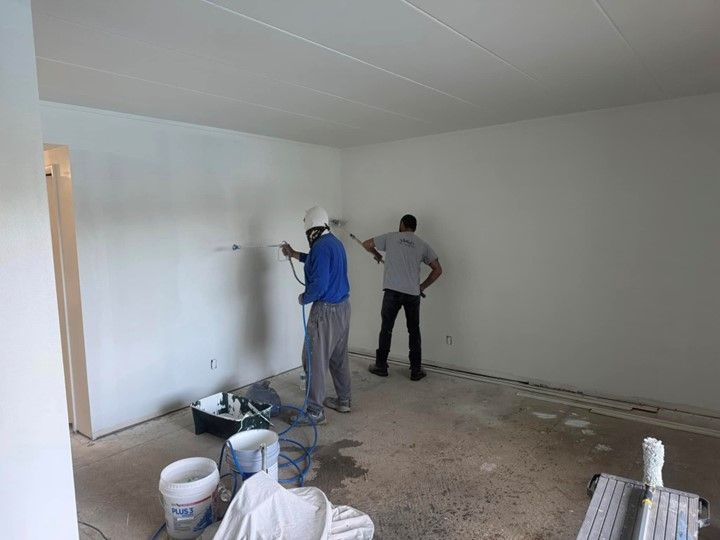Two men are painting a wall in a room.