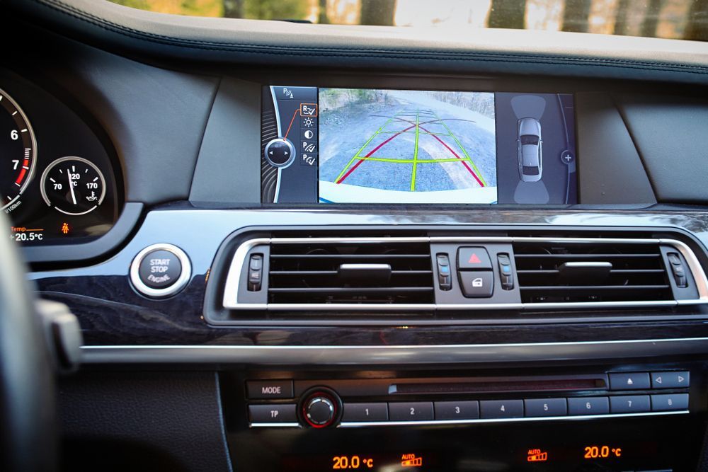Car interior view with reversing camera display, showing a vehicle's rear, green guidance lines, and dashboard details.
