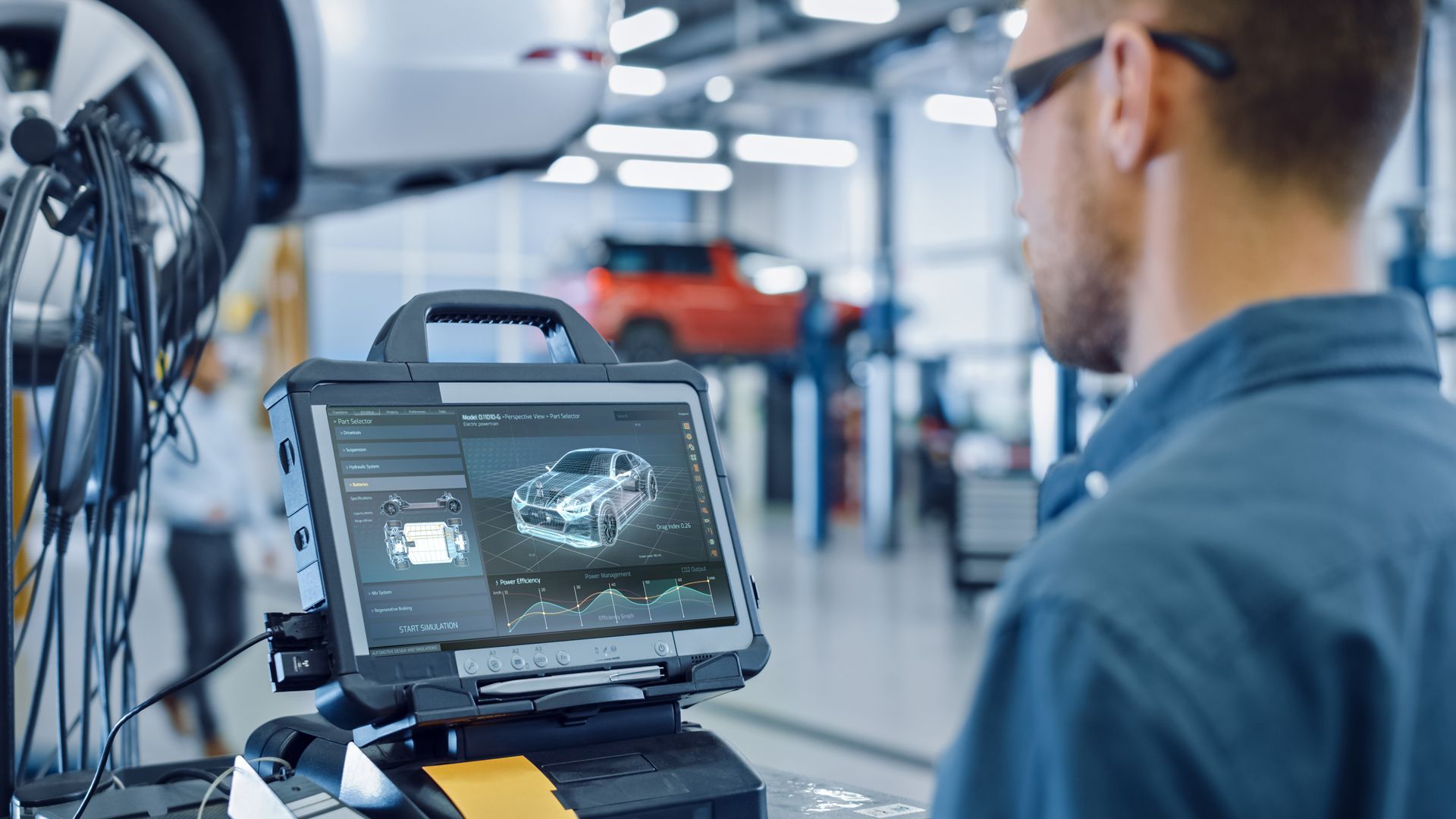 Mechanic using a tablet diagnostic tool in a car repair shop. A car is raised on a lift.