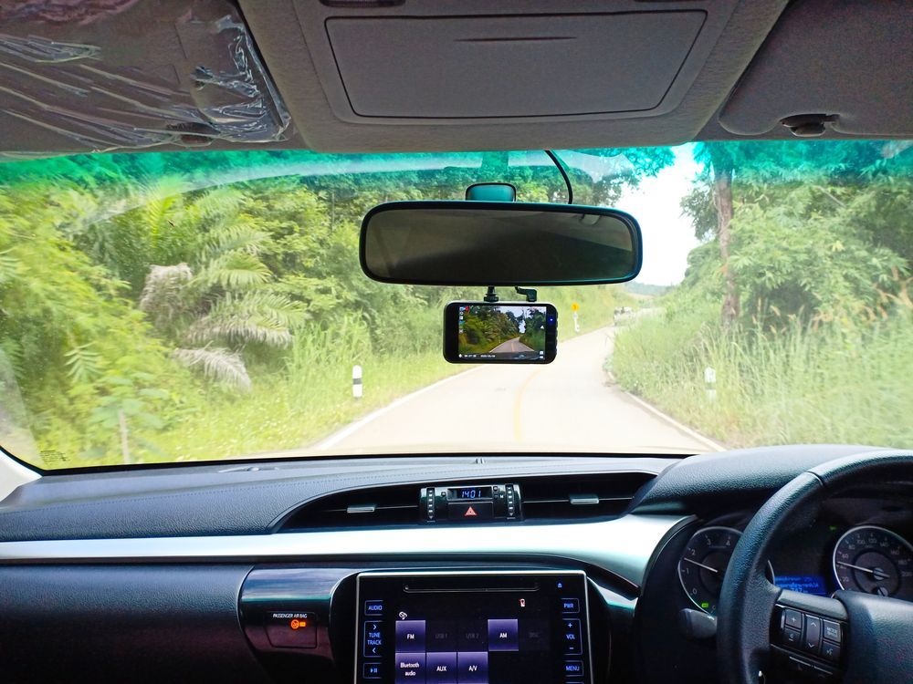 A car is driving down a dirt road with a rear view mirror.