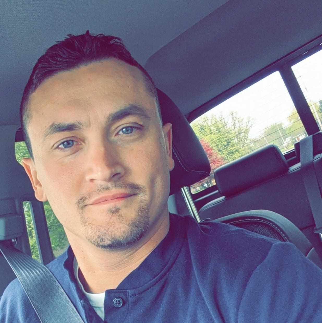 A man is taking a selfie in the back seat of a car