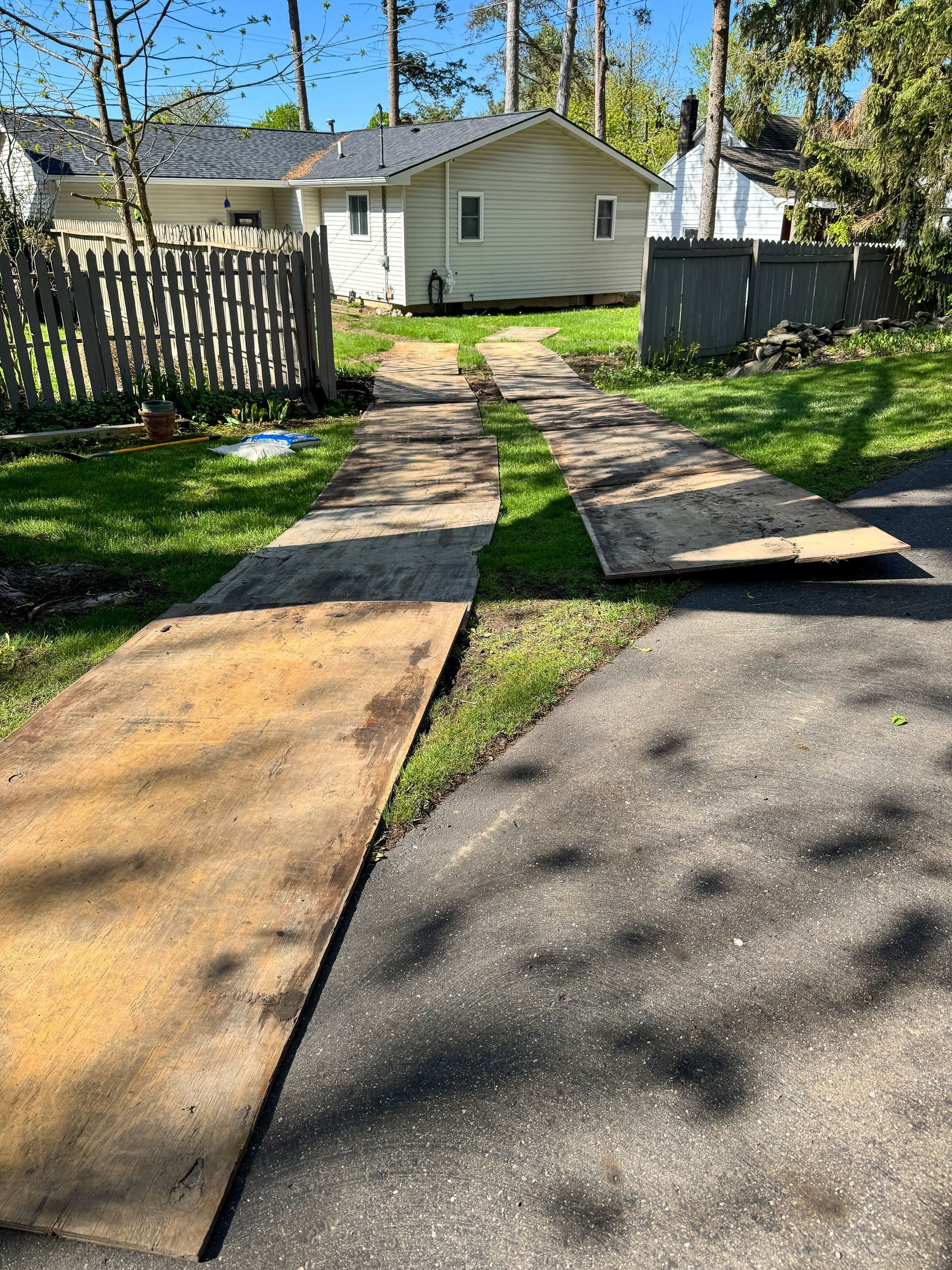 Concrete driveway with metal plates leading to a house, flanked by a wooden fence and grass.