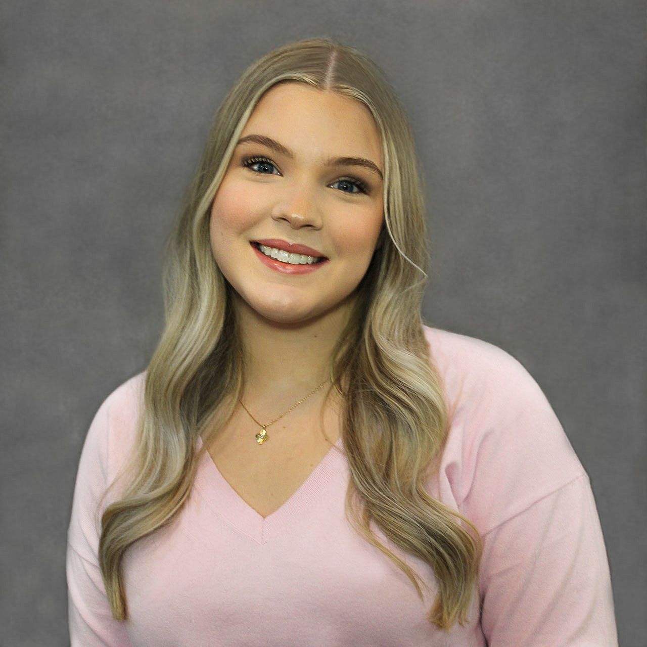 A young woman in a pink sweater is smiling for the camera.